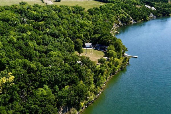Aerial view of a house and garage surrounded by dense trees on the shore of Pelican Lake. - 93100 25n Road, Pelican Lake