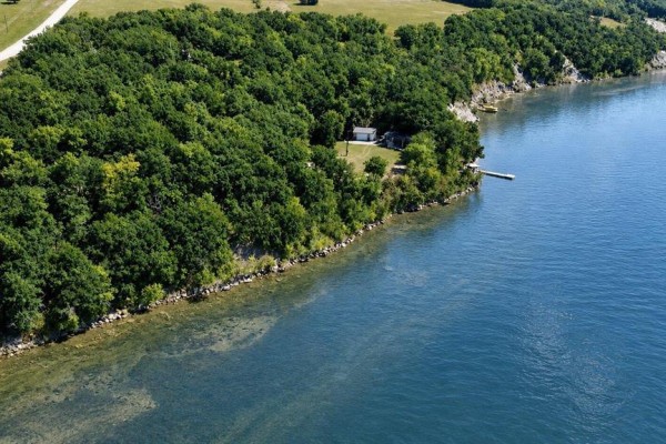Aerial view of a wooded property line meeting the clear water of Pelican Lake. - 93100 25n Road, Pelican Lake
