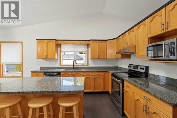 Corner view of the kitchen featuring wood cabinets, granite countertops, and a window. - 9323 69a Avenue, Grande Prairie