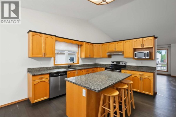 Kitchen island with seating, adjacent to wood cabinets and granite countertops. - 9323 69a Avenue, Grande Prairie