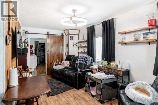 Living room with dark leather couches, a wooden dining table, and a sliding barn door. - 9324 101 Avenue, Grande Prairie
