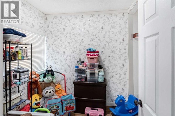 Bedroom with a bed, dark dresser, storage shelves, and stuffed animals. - 9324 101 Avenue, Grande Prairie