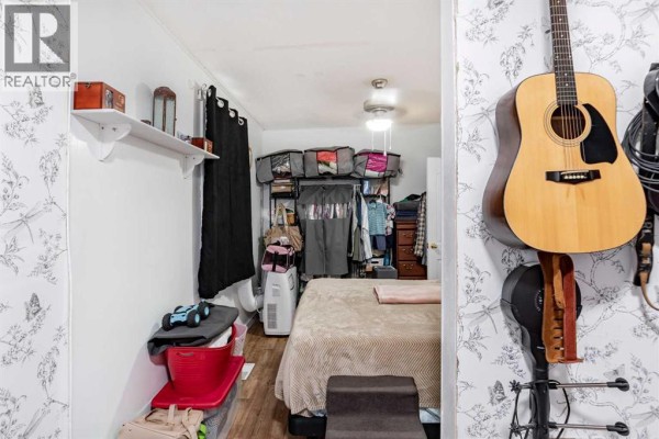 Bedroom with a bed, guitars on the wall, open closet with clothes, and patterned wallpaper. - 9324 101 Avenue, Grande Prairie