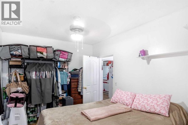 Bedroom with a bed, pink decorative pillows, open closet with clothes, and a door to another room. - 9324 101 Avenue, Grande Prairie
