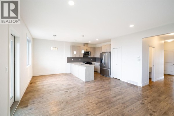 Open-concept living area with kitchen, large windows, and hardwood flooring - 933 Mt Robson Place Unit# 55, Vernon