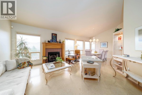 Living room with beige walls, a fireplace with a wooden mantle, large windows with a view, and beige flooring. - 933 Purcell Drive, Kelowna