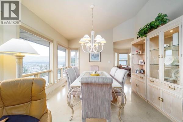 Dining room with a white chandelier, a dining table set for six, a china cabinet, and large windows with a view. - 933 Purcell Drive, Kelowna