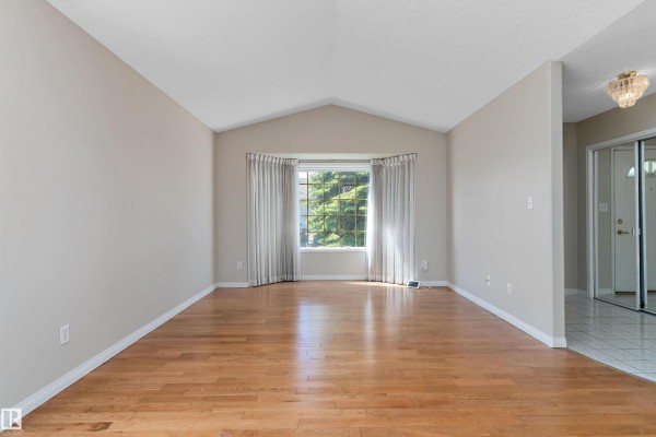 Living room with bay window and light beige walls, adjoining a tiled foyer and white door. - 933 Youville Dr W Nw, Edmonton