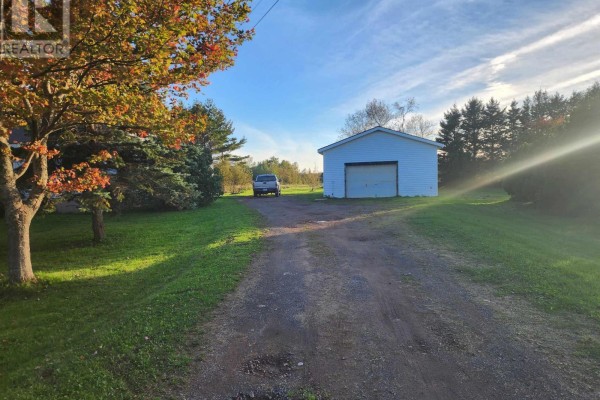 Gravel driveway leading to a white detached garage with a large roll-up door. - 9340 Highway 366, Port Howe