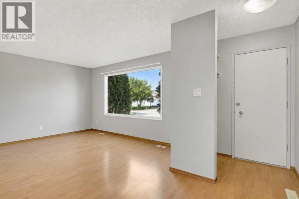 Entranceway with a gray partition wall, light wood flooring, and a white door. Shoes are visible on the floor. - 9343 112a Avenue, Grande Prairie