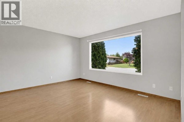 Living room with light wood laminate flooring, gray walls, and a large window overlooking the street and trees. - 9343 112a Avenue, Grande Prairie