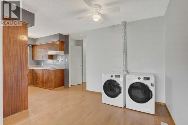 U-shaped kitchen with dark wood cabinets, light wood flooring, and white appliances. A built-in oven is visible on the left. - 9343 112a Avenue, Grande Prairie