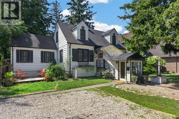 Front exterior of the white house with dark shutters, a small sunroom, and mature trees. - 935 Bartlet, Windsor