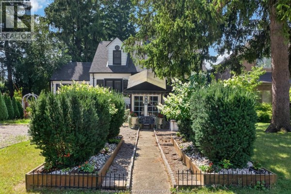 Concrete walkway through a lush garden with manicured bushes and flower beds leading to the entrance. - 935 Bartlet, Windsor