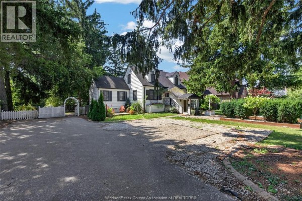 A driveway and lawn area in front of the white two-story house with trees. - 935 Bartlet, Windsor
