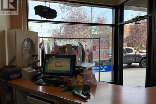 A computer and printer sit on the counter behind large front windows with clothes racks visible. - 935 General Avenue Ne, Calgary