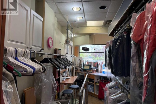 View of a dry cleaners with clothes on racks and a small desk with a stool. - 935 General Avenue Ne, Calgary