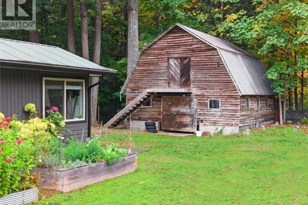 A rustic wooden barn with double doors and a sloped roof, next to a raised garden bed and a small building. - 936 Arden Rd, Courtenay