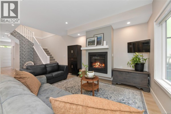 Living room with patterned wallpaper on stairs, black leather chair, grey sofa, and fireplace. - 937 Echo Valley Pl, Langford