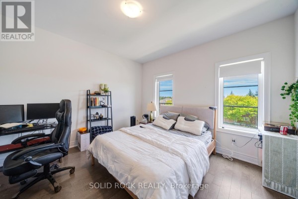 Bedroom with a bed, desk with dual monitors, and two windows overlooking trees. - 9376 Bayview Avenue, Richmond Hill