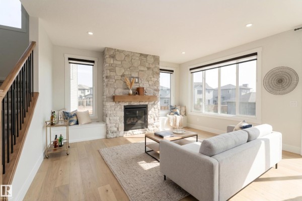 Living room with a stone fireplace, built-in window seats, grey sofa, and hardwood floors. - 9383 226 St Nw, Edmonton