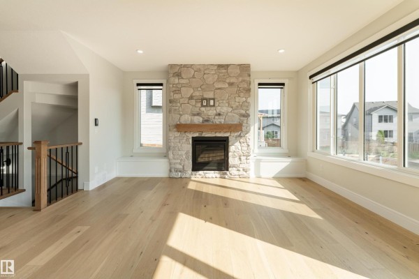 Spacious living room with a stone fireplace, large windows, and light wood floors, viewed from a corner. - 9383 226 St Nw, Edmonton