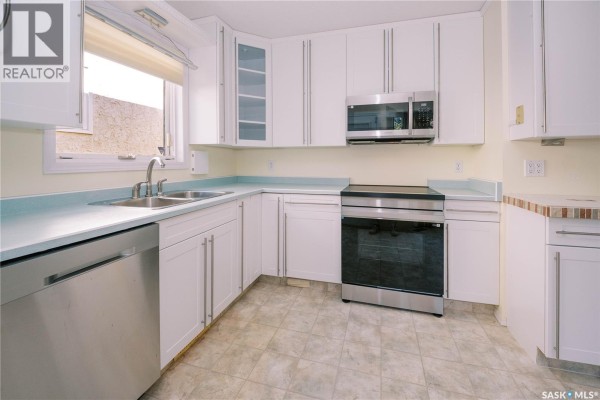 Corner kitchen with white cabinets, stainless steel appliances, and a light blue countertop. - 939 Haslam Crescent, Saskatoon