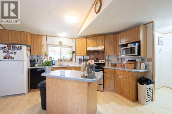 Kitchen with light wood cabinets, a central island with a grey countertop, and beige linoleum flooring. - 94, 5301 2 Street, Coalhurst