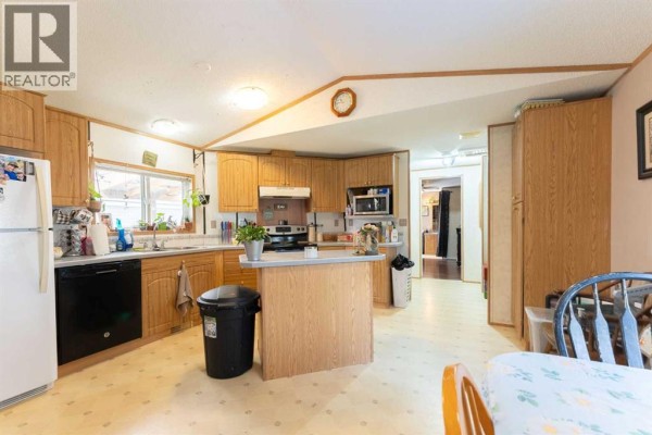 Kitchen with light wood cabinets, a central island, and a view into a hallway with a dining area. - 94, 5301 2 Street, Coalhurst