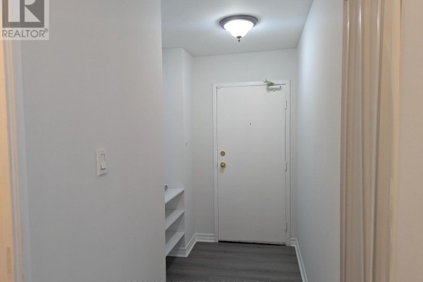 Interior view of a hallway with white walls, a grey door, and a small white shelving unit. - 94 - 2001 Bonnymede Drive, Mississauga