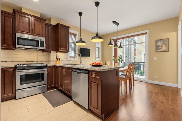 Kitchen with dark wood cabinets, granite counters, stainless steel appliances, and a small dining area. - 94 8068 207 Street, Langley