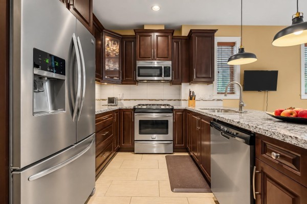 View of the kitchen showing a stainless steel refrigerator, dark wood cabinets, and granite countertops. - 94 8068 207 Street, Langley