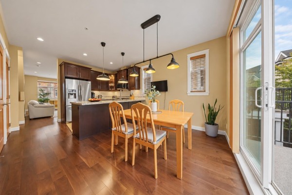 Dining area with a wooden table and chairs adjacent to the kitchen, with a sliding glass door. - 94 8068 207 Street, Langley