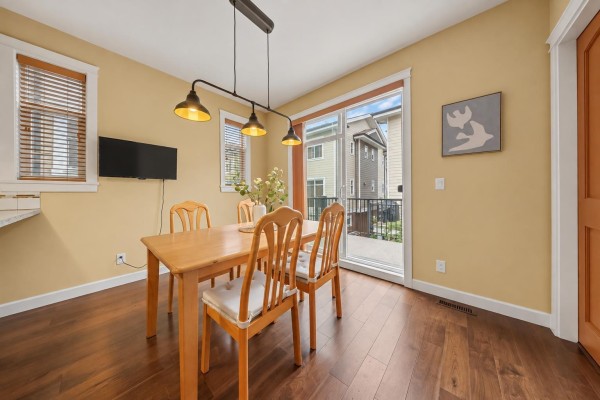 Dining area with a wooden table, chairs, and a sliding glass door overlooking a backyard. - 94 8068 207 Street, Langley