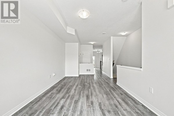 Interior view of a wide, empty room with light grey laminate flooring and white walls, showing access to stairs. - 94 Laguna Village Crescent, Hamilton