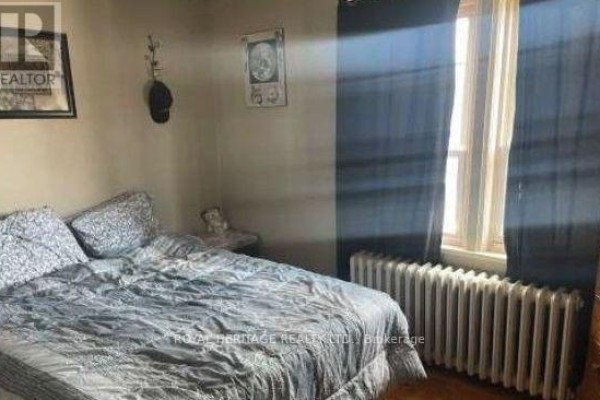 Bedroom with a queen-size bed, patterned pillows, dark blue curtains, and a radiator. - 94 Lake Street, St  Catharines