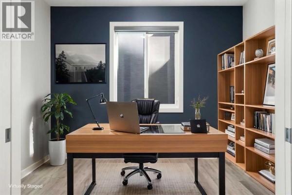 Home office with a wooden desk, chair, laptop, bookshelf, and dark blue walls. - 94 Mahogany Cove Se, Calgary