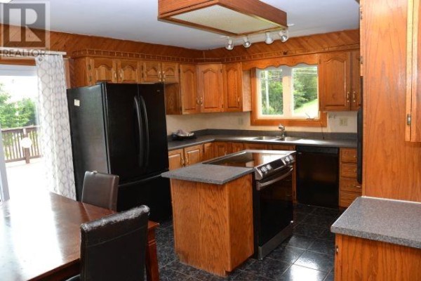 Wood-paneled kitchen with oak cabinets, black appliances, an island, and dark tiled floor. - 94 Main Road, Aquaforte