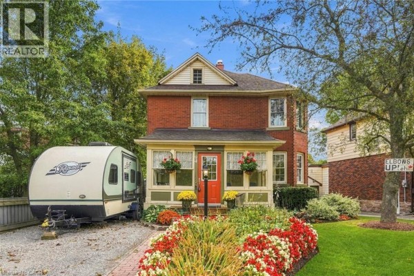 Red brick two-story house with a covered porch and flower beds lining the walkway. - 94 River Road, Welland