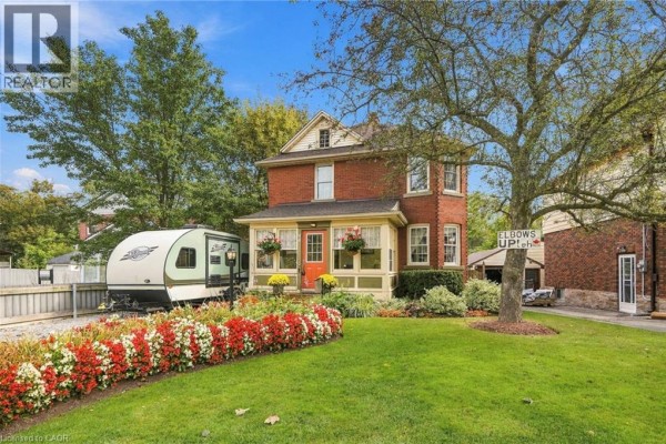 Exterior of a red brick house with a neatly manicured lawn and flower beds. - 94 River Road, Welland