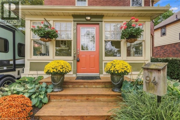 Front entrance of a house with wooden steps, red door, large windows, and potted yellow mums. - 94 River Road, Welland