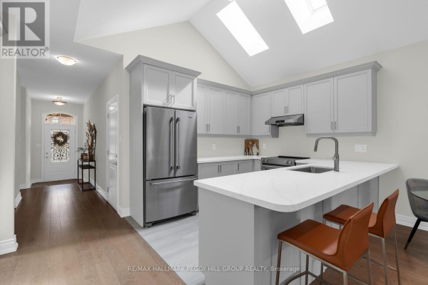 Modern kitchen with light grey cabinets, stainless steel appliances, and vaulted ceiling with skylights. - 94 Summerhill Drive, New Tecumseth