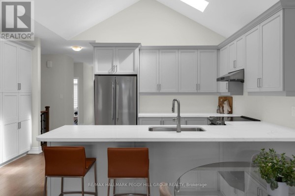 Kitchen island with quartz countertop, stainless steel sink, and two brown bar stools. - 94 Summerhill Drive, New Tecumseth