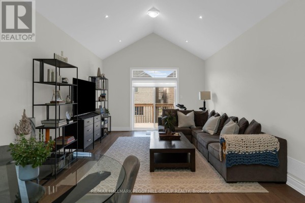 Living room with vaulted ceiling, dark brown sectional sofa, coffee table, and large sliding glass doors. - 94 Summerhill Drive, New Tecumseth