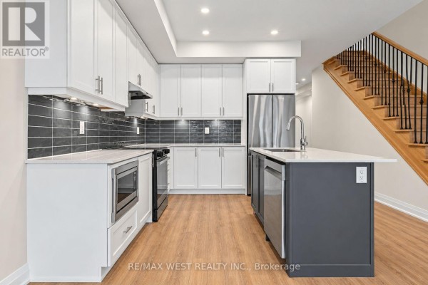 Modern kitchen with white cabinets, dark gray backsplash, stainless steel appliances, and an island. - 94 Sunshine Lane, Orillia