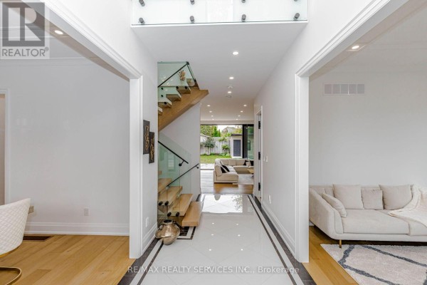 Hallway with a glass-railed staircase, hardwood floors, and views into the backyard and living area. - 94 Vista Boulevard, Mississauga
