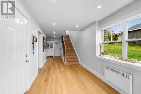 Hallway showing a wooden staircase, white doors, built-in cabinet, and windows overlooking the yard. - 94 Water's Edge Lane, Cornwall