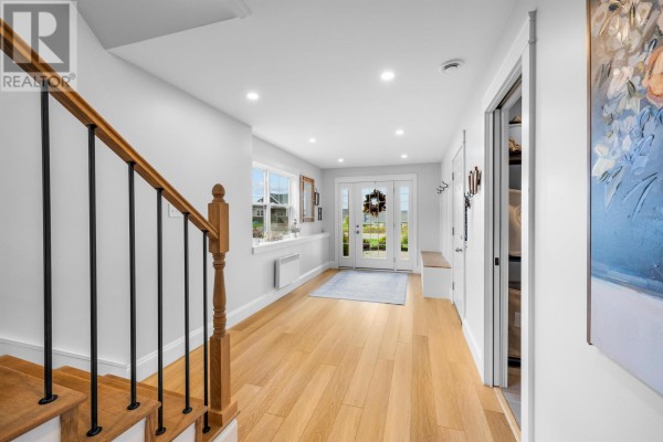 View down the bright hallway towards the double glass doors and entryway staircase with black spindles. - 94 Water's Edge Lane, Cornwall