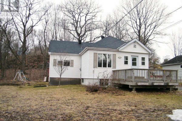 White house exterior with wooden deck, bare trees and patchy snow on lawn. - 94 William Street, Parry Sound