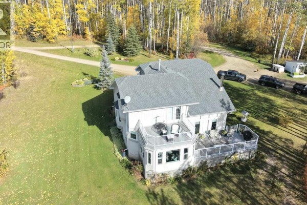 Rear exterior of a house with a wrap-around deck and a sunroom addition, surrounded by trees and lawn. - 94038b -- 702 Township, Rural Grande Prairie No  1, County Of